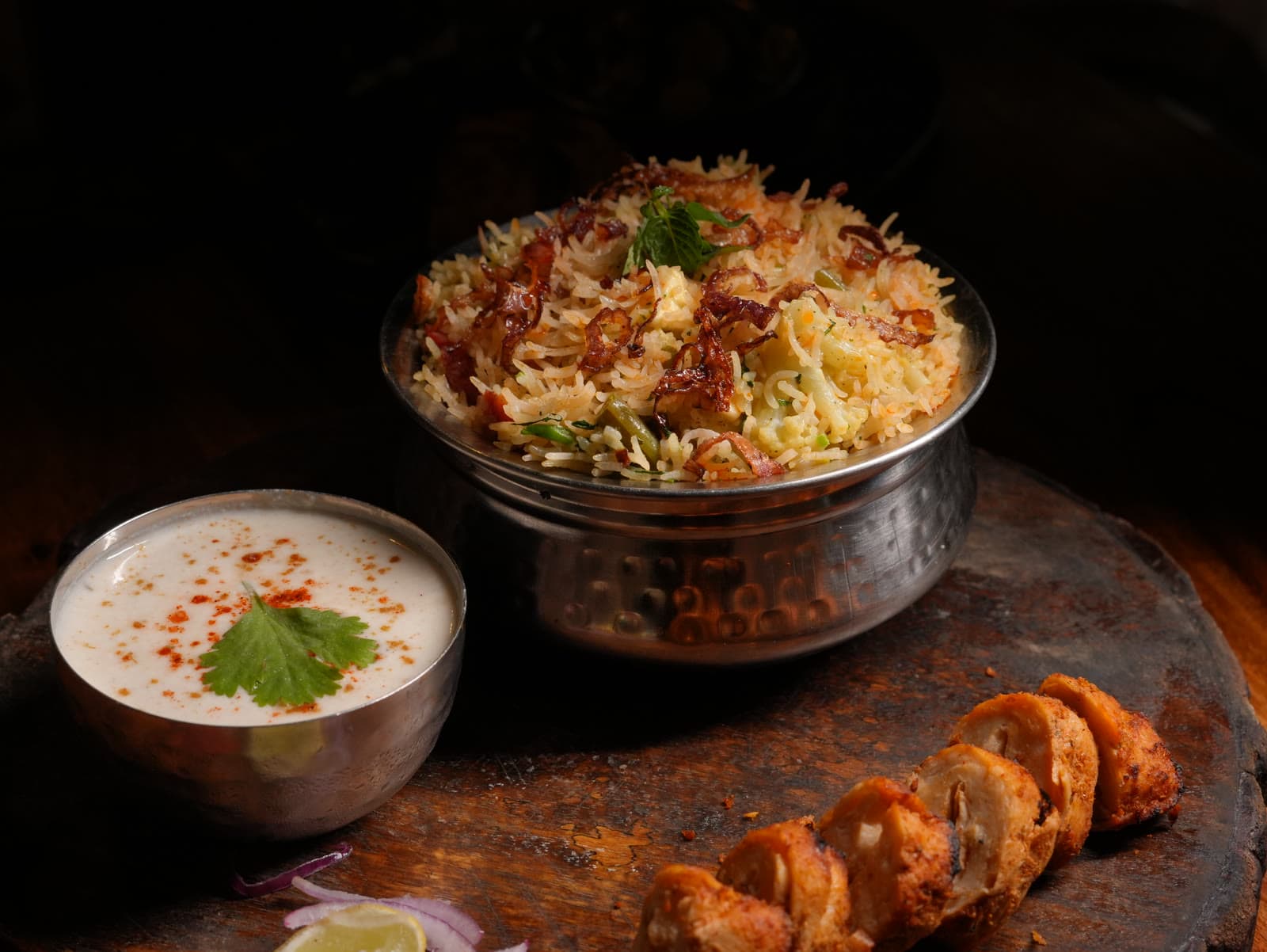 Dum biryani in a copper handi with raita and seekh kebab